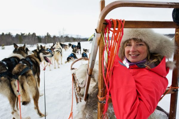 En kvinne koser seg som passasjer på hundekjøring i Nord-Norge